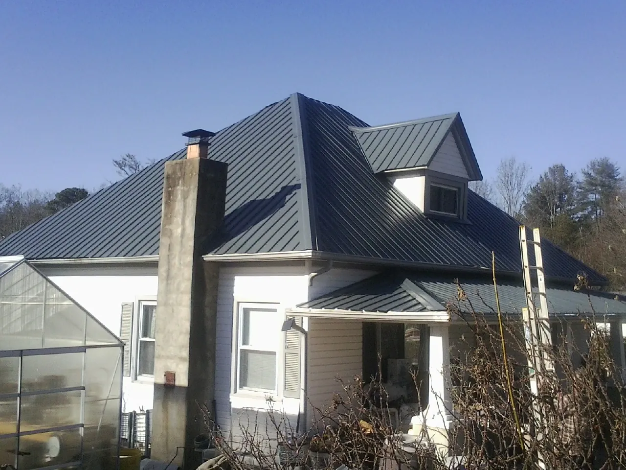 Dark blue standing seam metal roof on a white farmhouse with dormer — Slate & Tile Roof Repair by Roofing Brothers in Alvo
