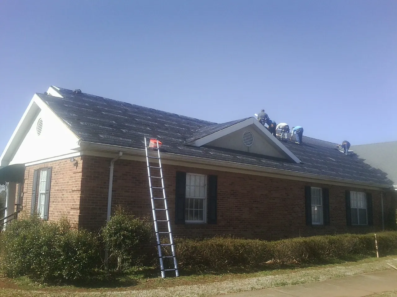 Crew tearing shingles off a brick ranch roof with a ladder set — Metal Roof Repair work by our crew in Alvo