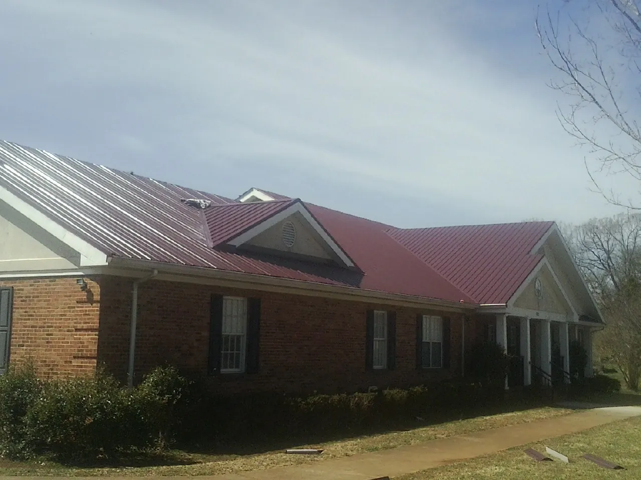 Red metal roof with gabled entries on a long brick building, from a Hail Damage Roof Repair job in Alvo