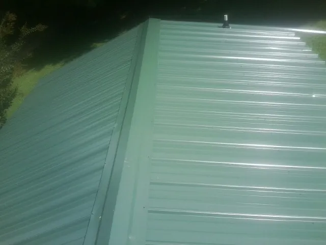 New green metal panels meeting at the ridge of a roof — Flat Roof Repair work by our crew in Alvo