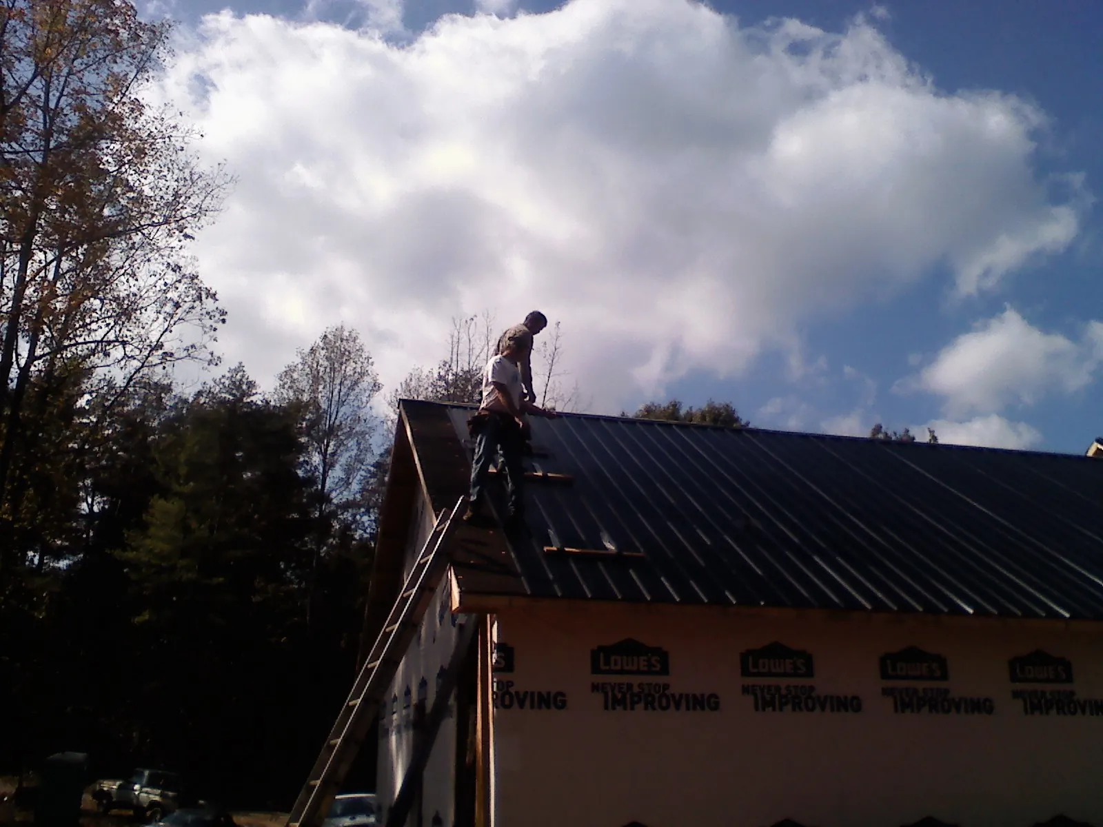 Roofer fastening dark metal panels high against a cloudy sky, from a Roof Inspection job in Alvo