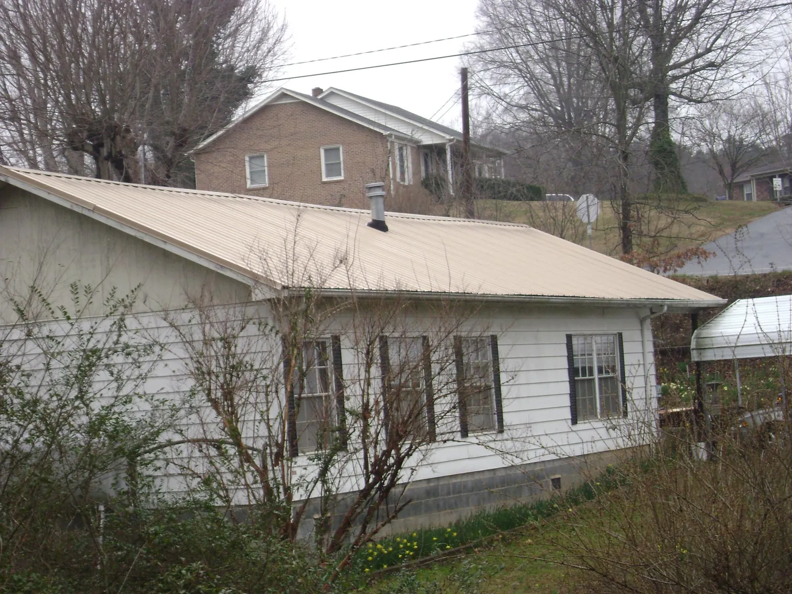 Tan metal roof on a white sided house set into a hillside — Commercial Roofing by Roofing Brothers in Alvo